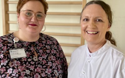 Caroline Runge, Abteilungsleitung Pflege, und PD Dr. Anna Christina Alegiani, Oberärztin der neurologischen Frührehabilitation, stehen lächelnd nebeneinander im Klinikum Altona. Runge trägt ein geblümtes Kleid, Alegiani einen weißen Arztkittel mit Asklepios-Logo.