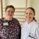 Caroline Runge, Abteilungsleitung Pflege, und PD Dr. Anna Christina Alegiani, Oberärztin der neurologischen Frührehabilitation, stehen lächelnd nebeneinander im Klinikum Altona. Runge trägt ein geblümtes Kleid, Alegiani einen weißen Arztkittel mit Asklepios-Logo.