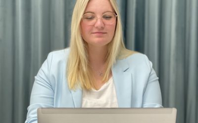 Frau arbeitet konzentriert am Laptop im Büro, mit Tasse und Smartphone auf dem Tisch.