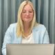 Frau arbeitet konzentriert am Laptop im Büro, mit Tasse und Smartphone auf dem Tisch.
