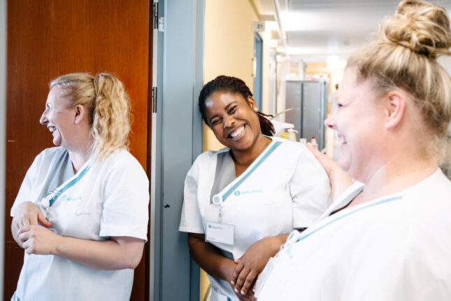 Drei Pflegekräfte der Asklepios Klinik lachen gemeinsam auf dem Flur während ihrer Schicht.