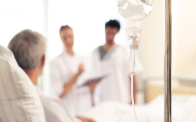 Pflegekräfte sprechen mit einem älteren Patienten auf der Palliativstation, Infusion im Vordergrund.