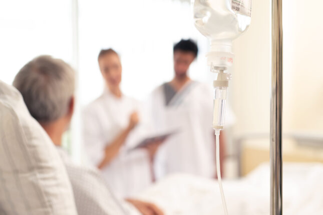 Pflegekräfte sprechen mit einem älteren Patienten auf der Palliativstation, Infusion im Vordergrund.