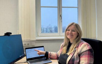 Mitarbeitende bei Asklepios zeigt am Arbeitsplatz im Büro auf Laptop mit Präsentation zu Nachhaltigkeit und Digitalisierung im Gesundheitswesen.