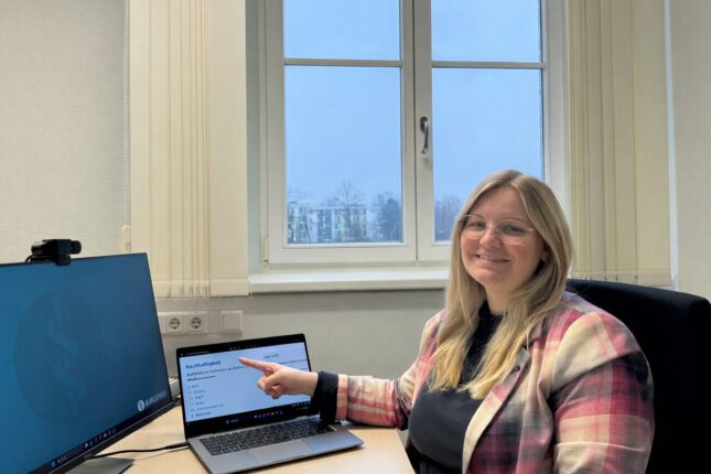 Mitarbeitende bei Asklepios zeigt am Arbeitsplatz im Büro auf Laptop mit Präsentation zu Nachhaltigkeit und Digitalisierung im Gesundheitswesen.