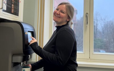Lächelnde Asklepios-Mitarbeitende steht in einem hellen Pausenraum am Kaffeevollautomaten und hält eine Tasse.